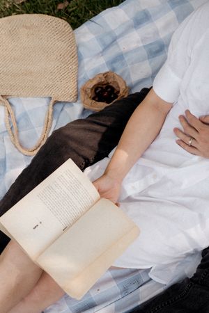 A person lying down reading a book on a blue and white checkered blanket in soft natural light.