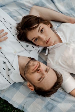 A couple lying on a blue checkered blanket in white clothing outdoors.