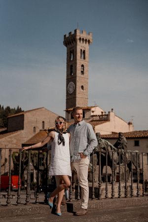 Couple poses in front of historic Italian tower and buildings in Fiesole during sunset.