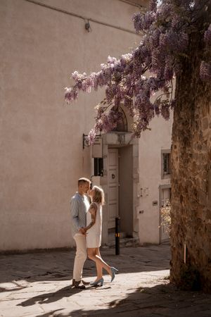A couple sharing tender moments under blooming trees in sunlit courtyard in Fiesole, Italy.