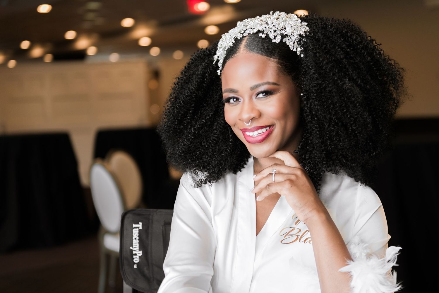 Radiant Black bride wearing pearl headband and white robe smiling in wedding venue.