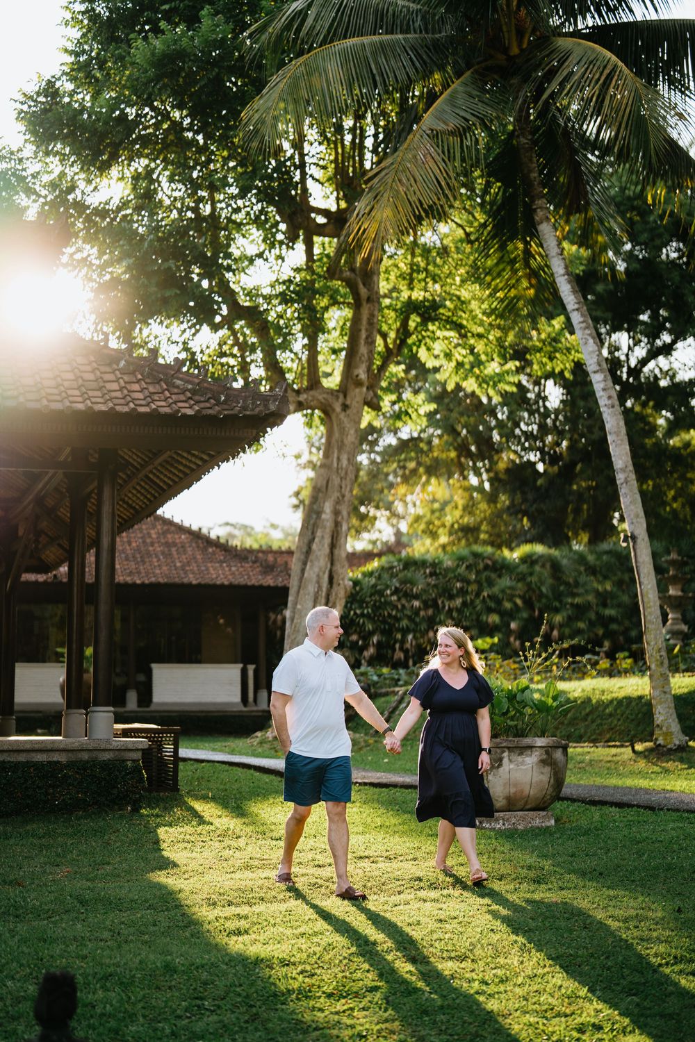 People walking on green lawn near palm trees and traditional architecture at sunset.