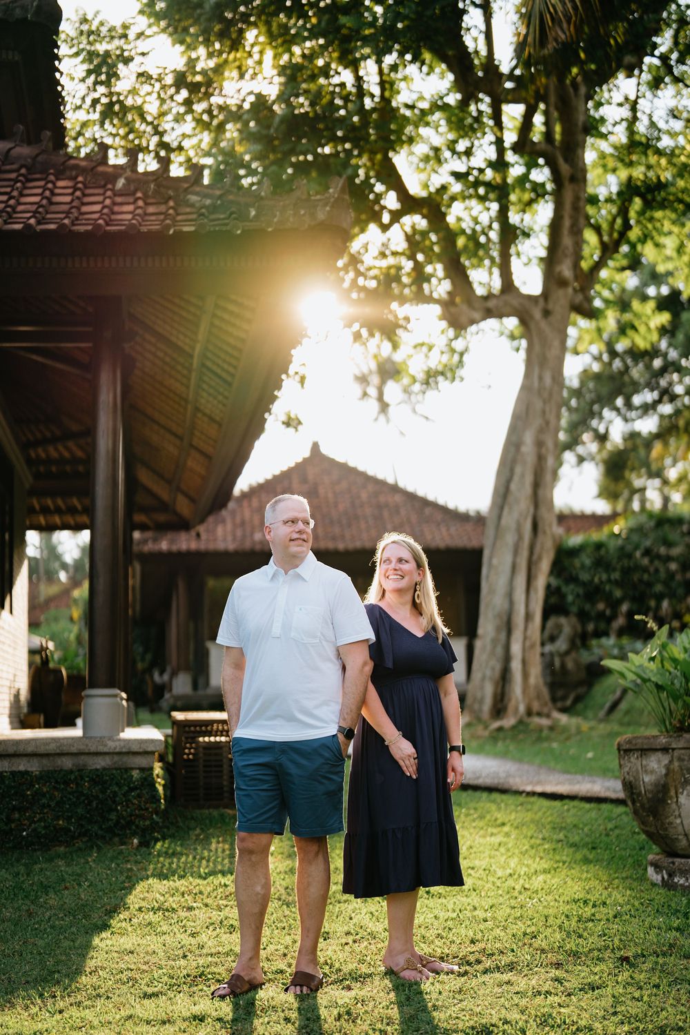 Family photoshoot in a tropical garden with traditional buildings and palm trees.
