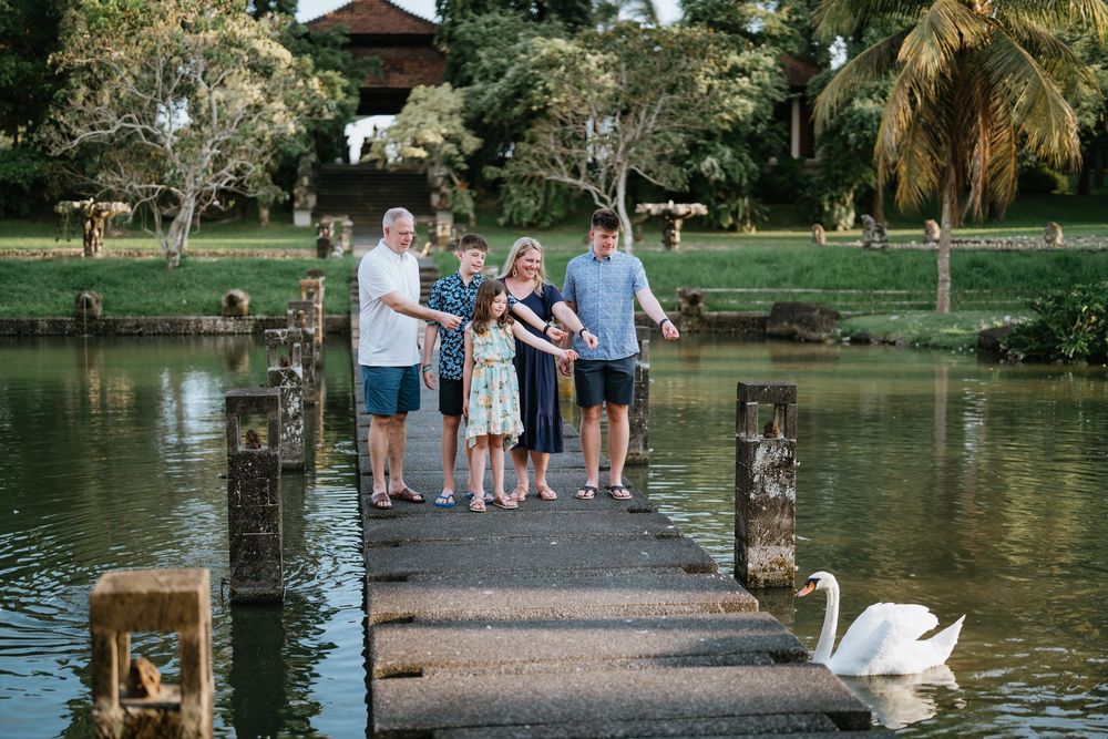 Family walking along a lakeside path with swans swimming nearby.