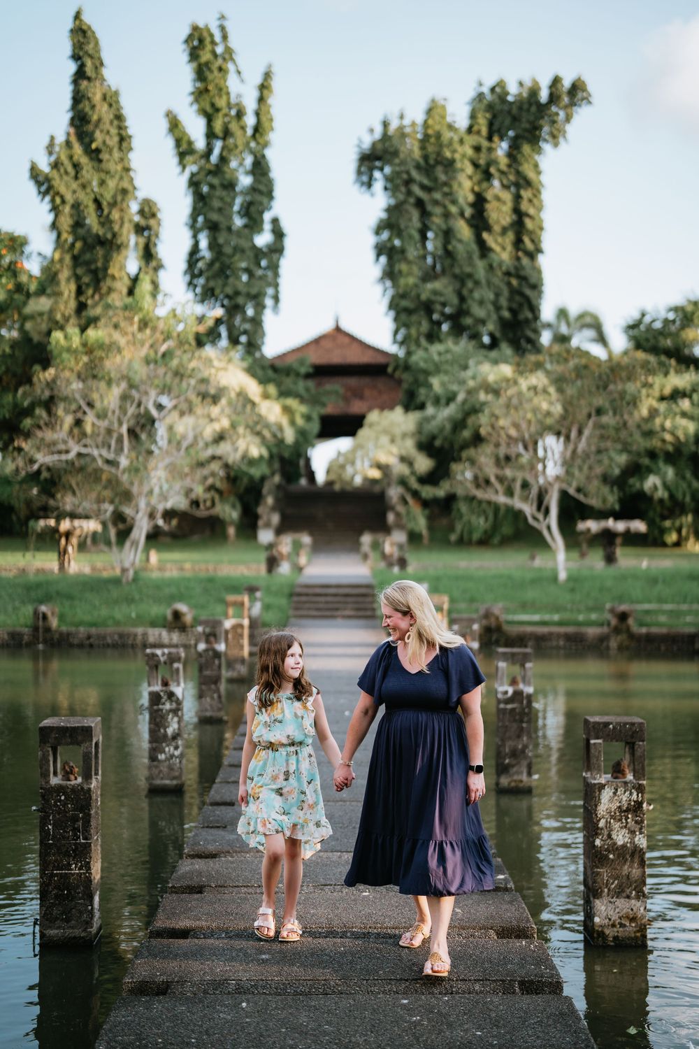 People standing on wooden pier overlooking tranquil lake with palm trees in background.