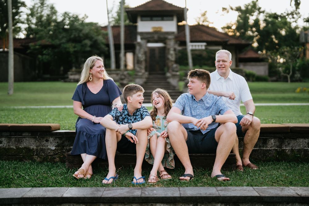 A family sits together on stone steps with a traditional Asian building visible in the background.