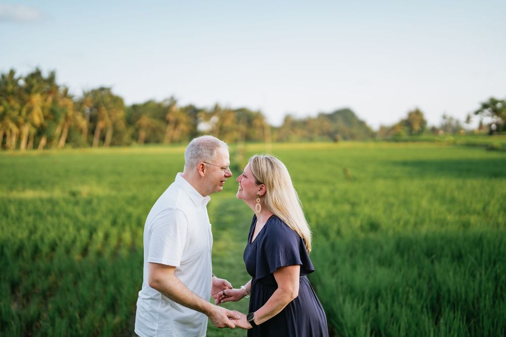 A couple shares an intimate moment while standing in a lush green field at sunset.