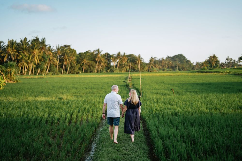 Two people walk along a narrow path through vibrant green rice fields at sunset.