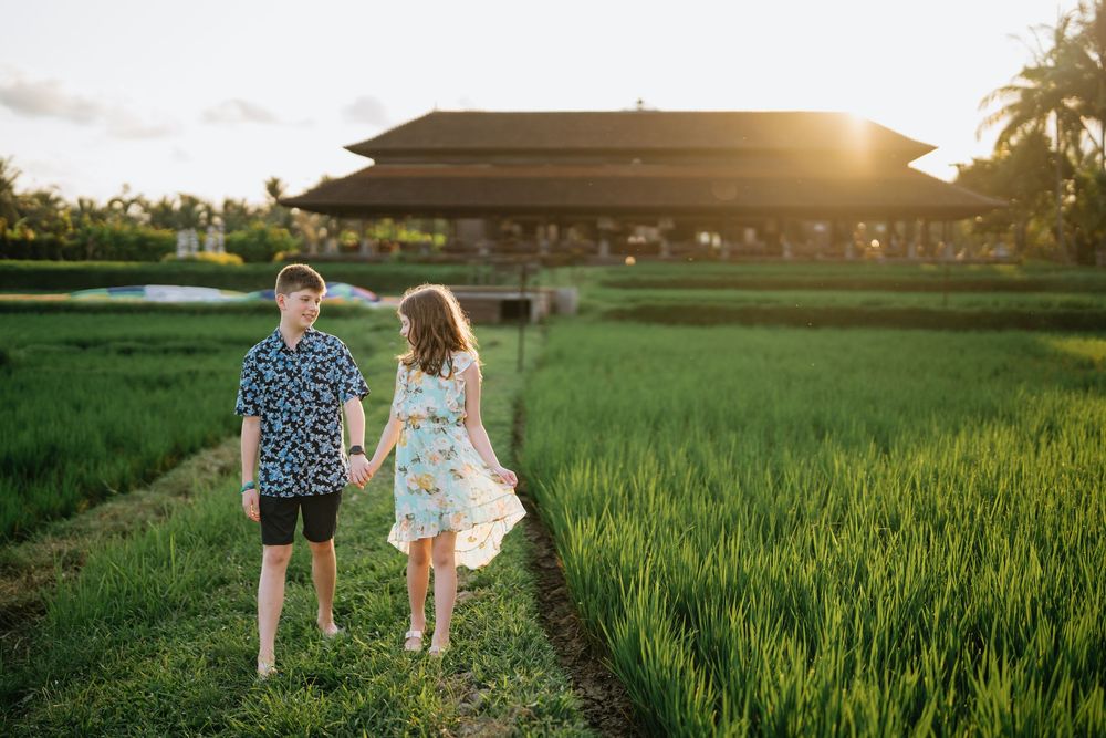 A couple strolls through verdant rice paddies with a traditional Balinese building in the golden sunset.