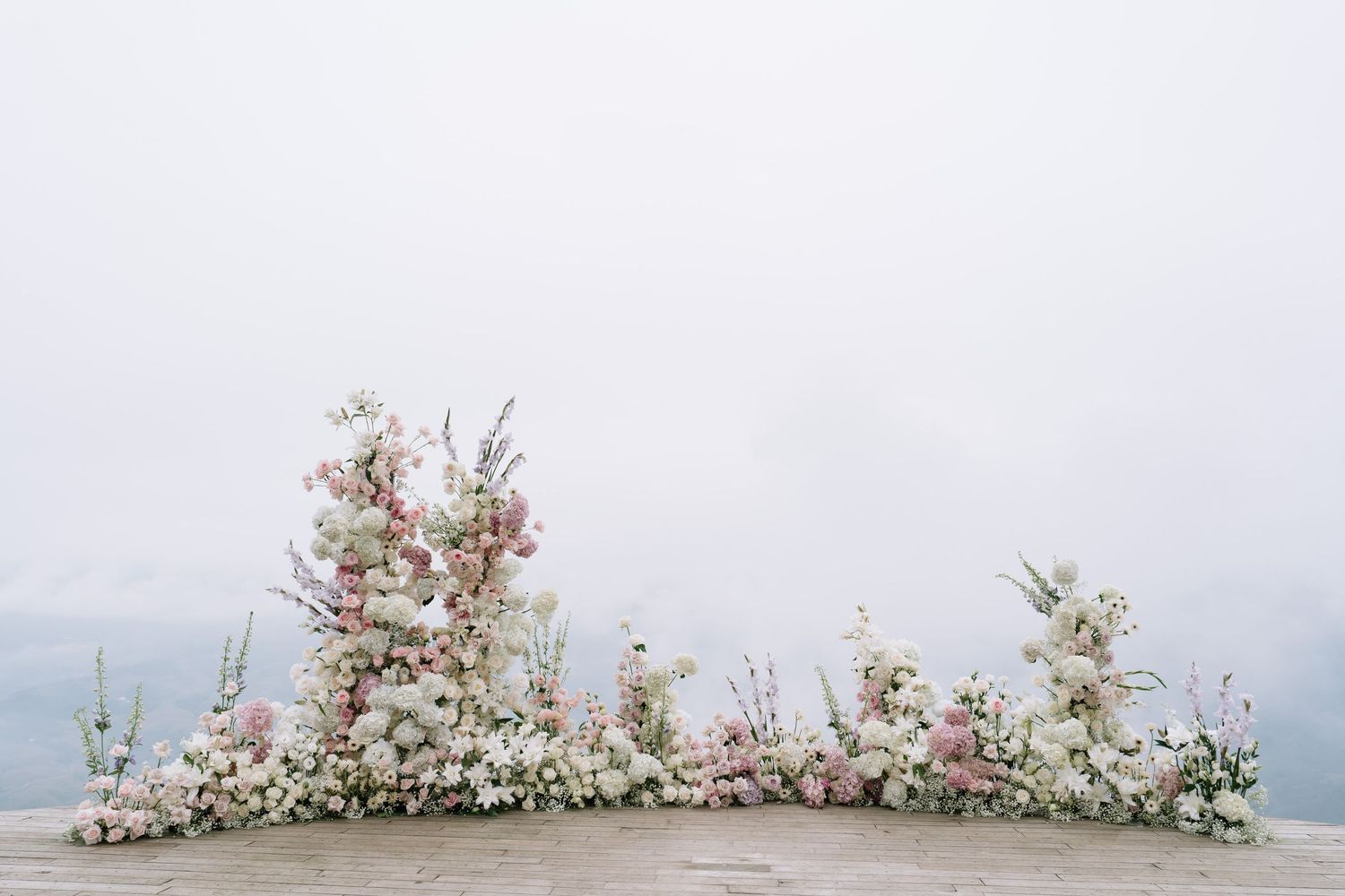 Romantic white and pink wedding floral display arranged on stone ground with misty background.