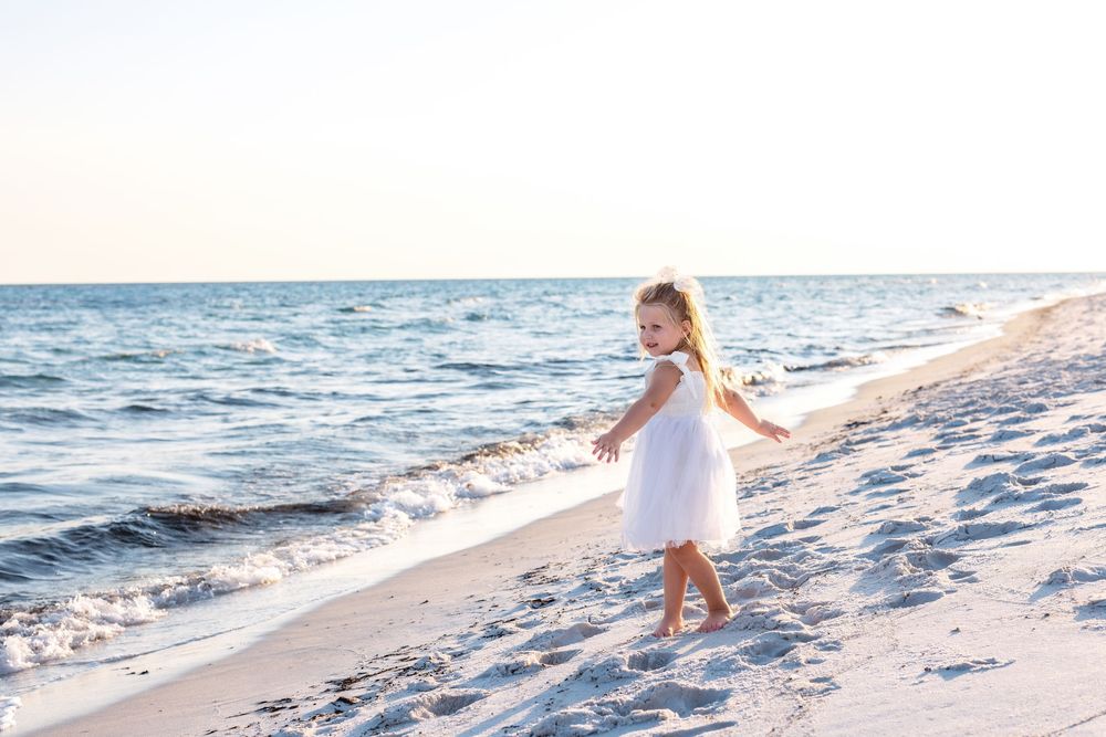 Light summer dress flows in the ocean breeze as waves lap against the sandy shoreline at sunset.