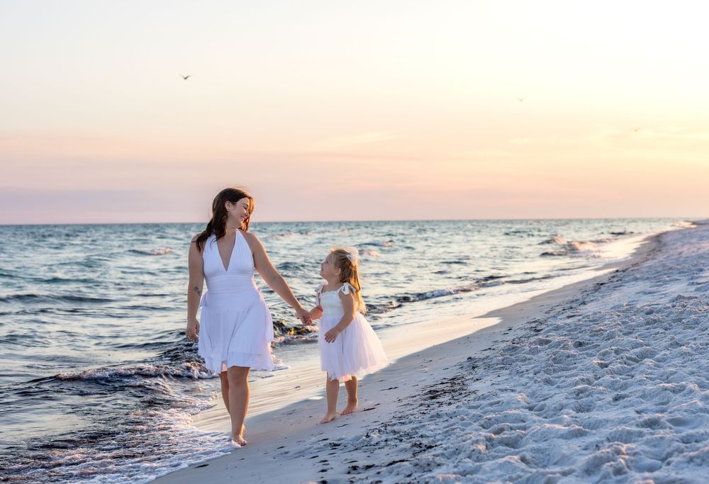 Family wearing white walks along pristine beach at sunset with gentle waves lapping at sandy shore.