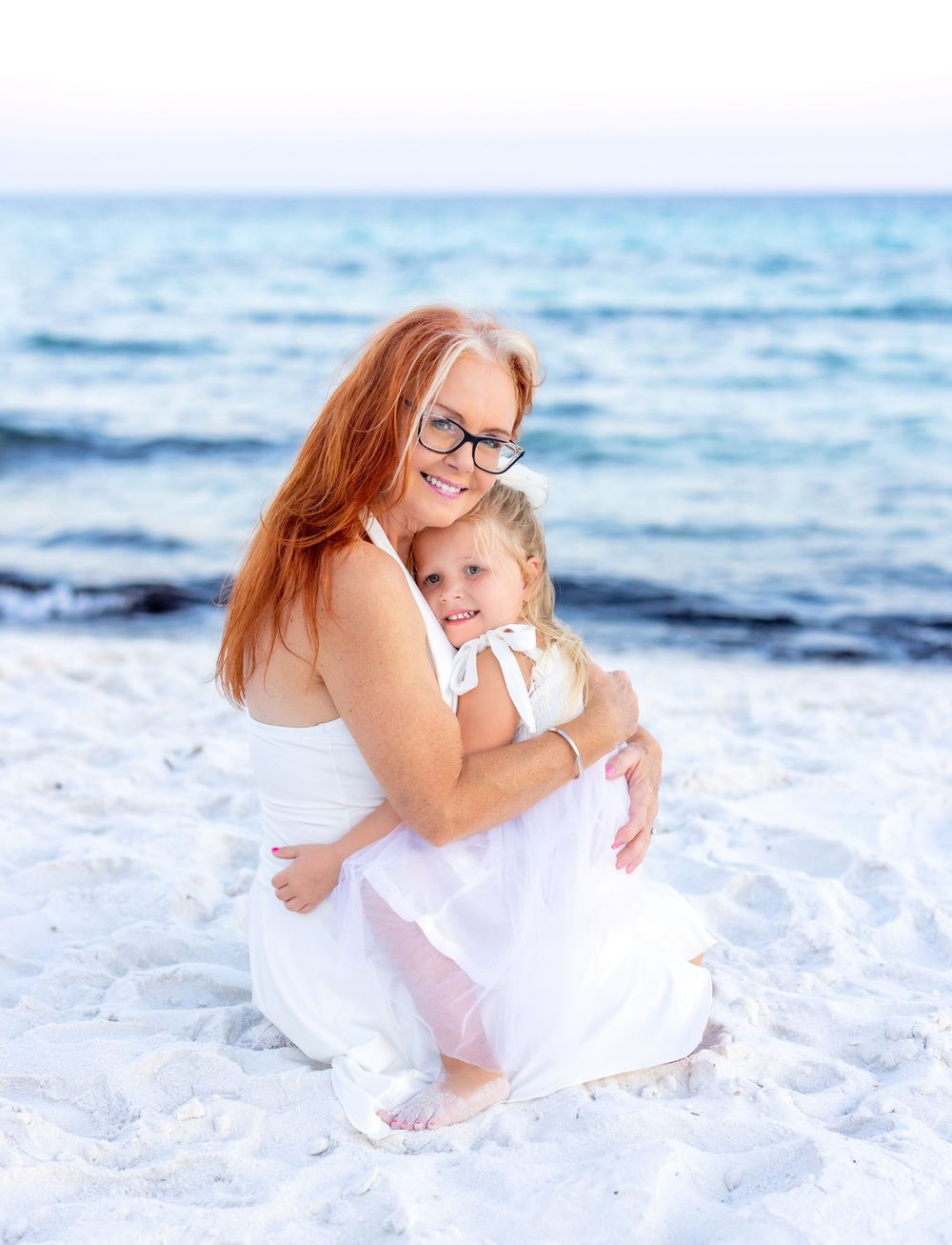Joyful beachside family photos captured in white outfits against sparkling ocean waves and sand.