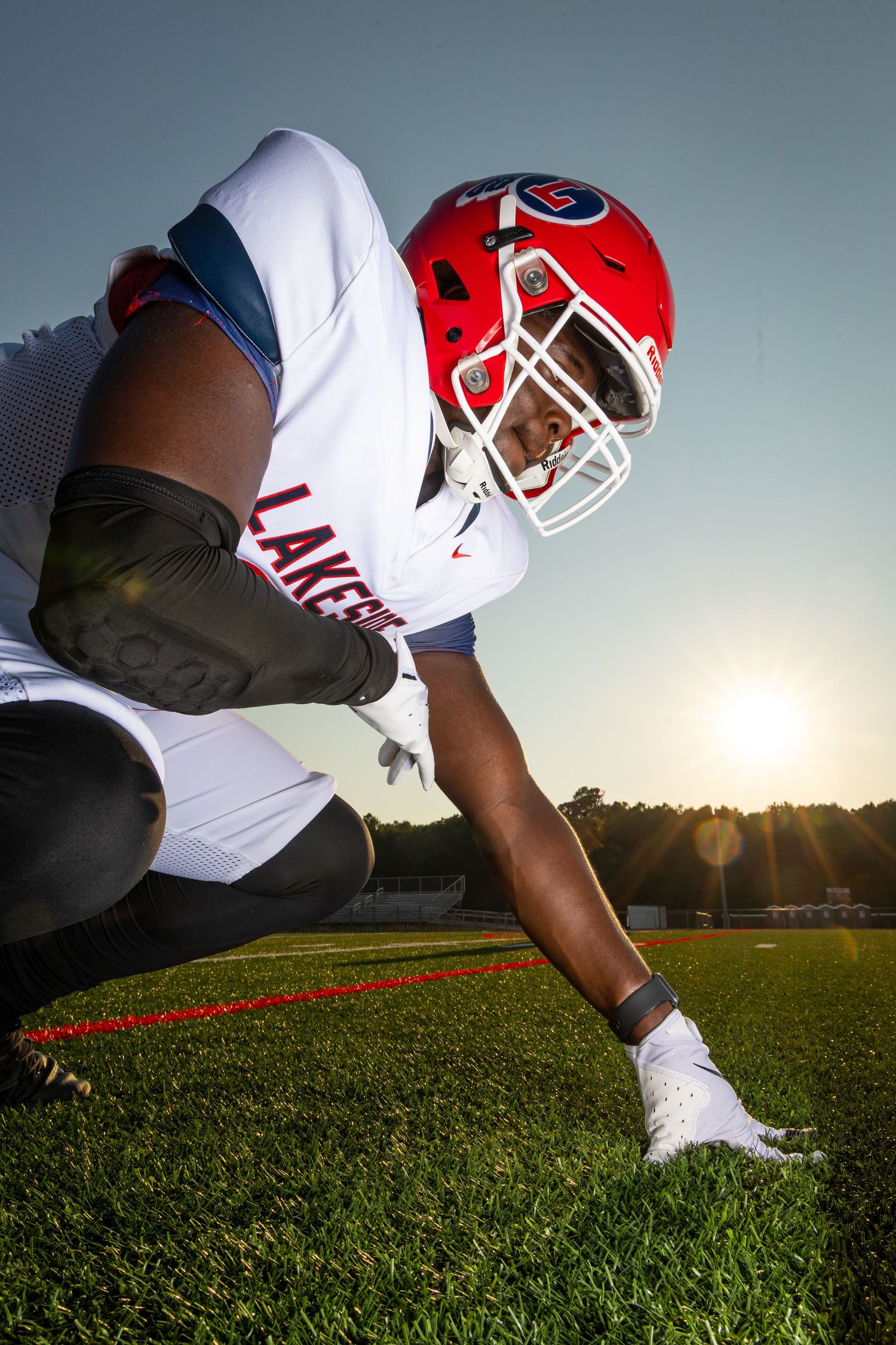 Close-up views of a football player crouched on artificial turf at field level during sunset in uniform and gear.