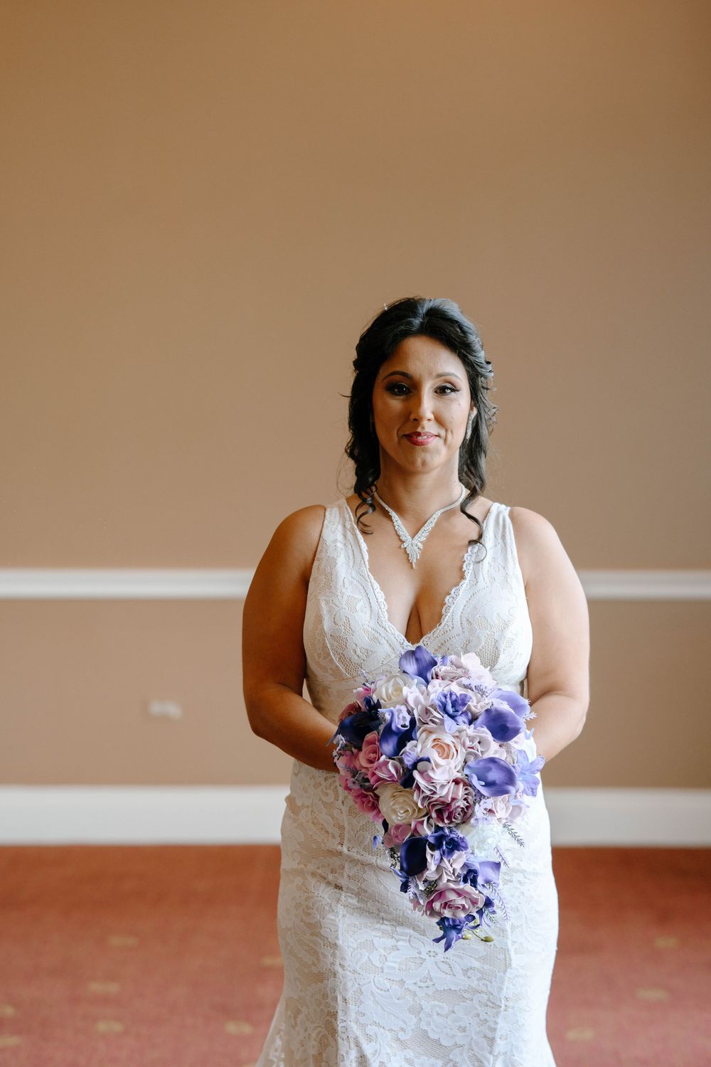 Beautiful bride in a white lace dress holding a stunning purple and pink floral bouquet.