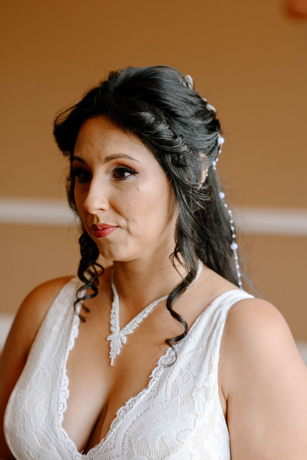 Bride wearing white lace halter dress with curled dark hair styled elegantly for her wedding day.