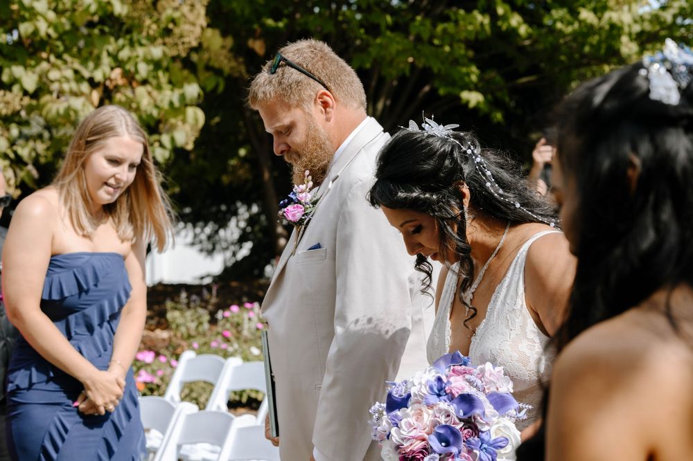 Outdoor wedding ceremony setup with floral arrangements and guests seated under trees.