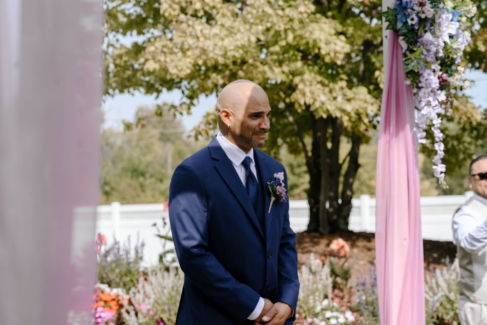 Elegant outdoor wedding ceremony with guests seated in rows on a sunny day surrounded by trees and pink draping.
