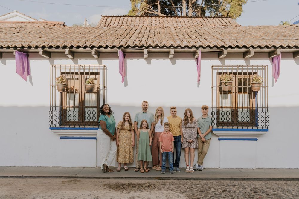 A group stands in front of a white stucco building with wrapped arched columns during an outdoor photo session.