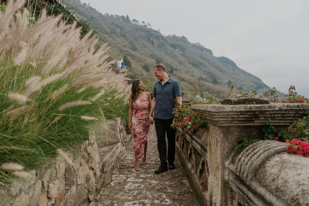 Couple sharing a romantic moment on a scenic stone terrace surrounded by lush greenery and misty mountains.
