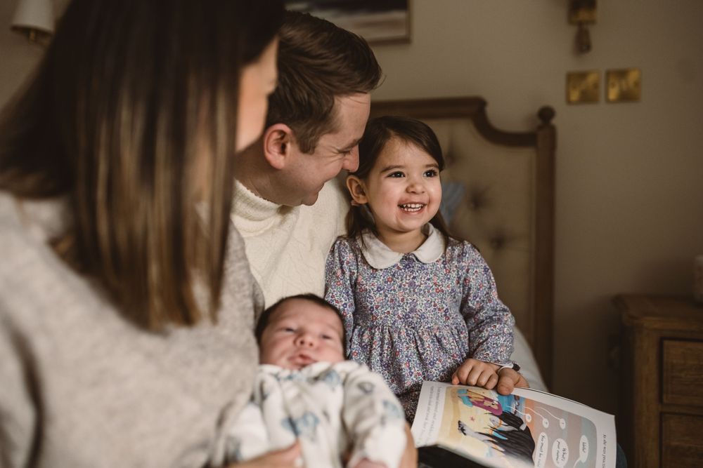 Family with a newborn baby and toddler share tender moments together in a cozy indoor setting during a relaxed photo session.
