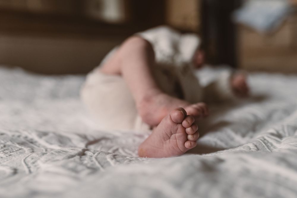Close up of baby feet and toes shown on white blanket with delicate patterns.