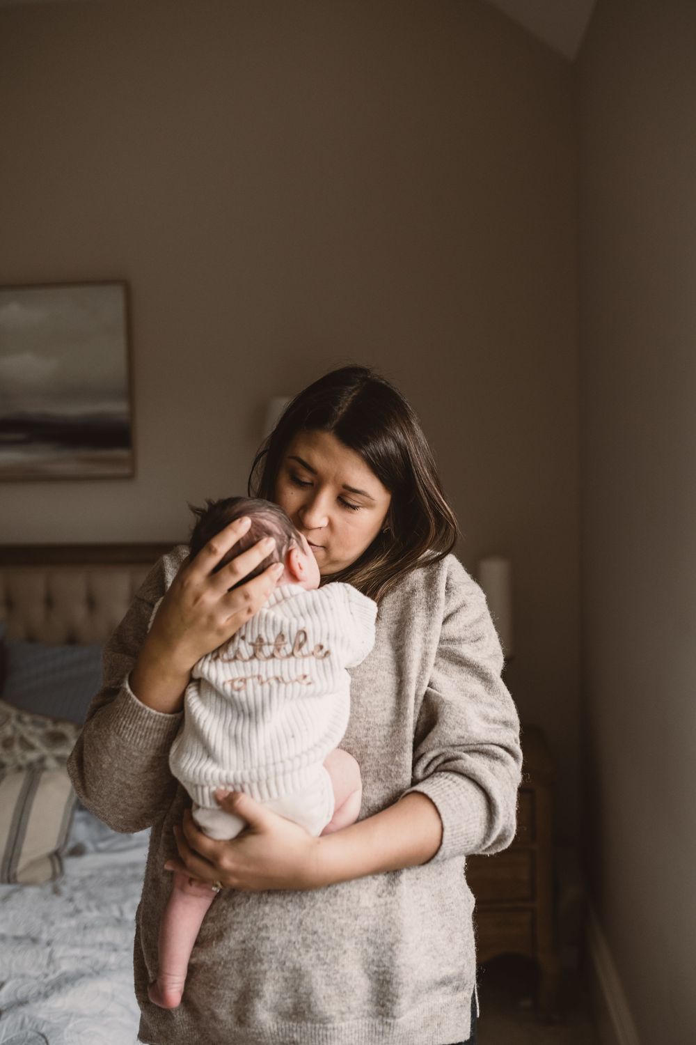 Mother holding sleeping newborn baby in natural light with cozy gray sweater.