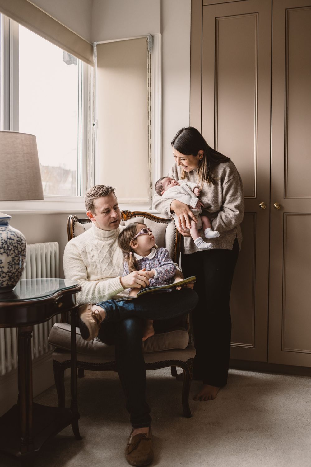 Family of four with a newborn baby and toddler interacting in a home setting.