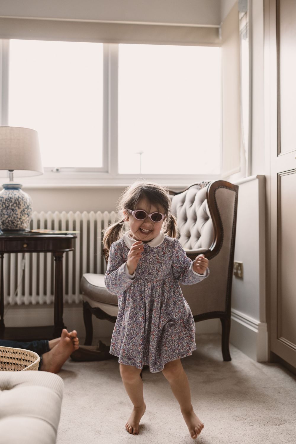 A child in a floral dress dances playfully in a bright room.