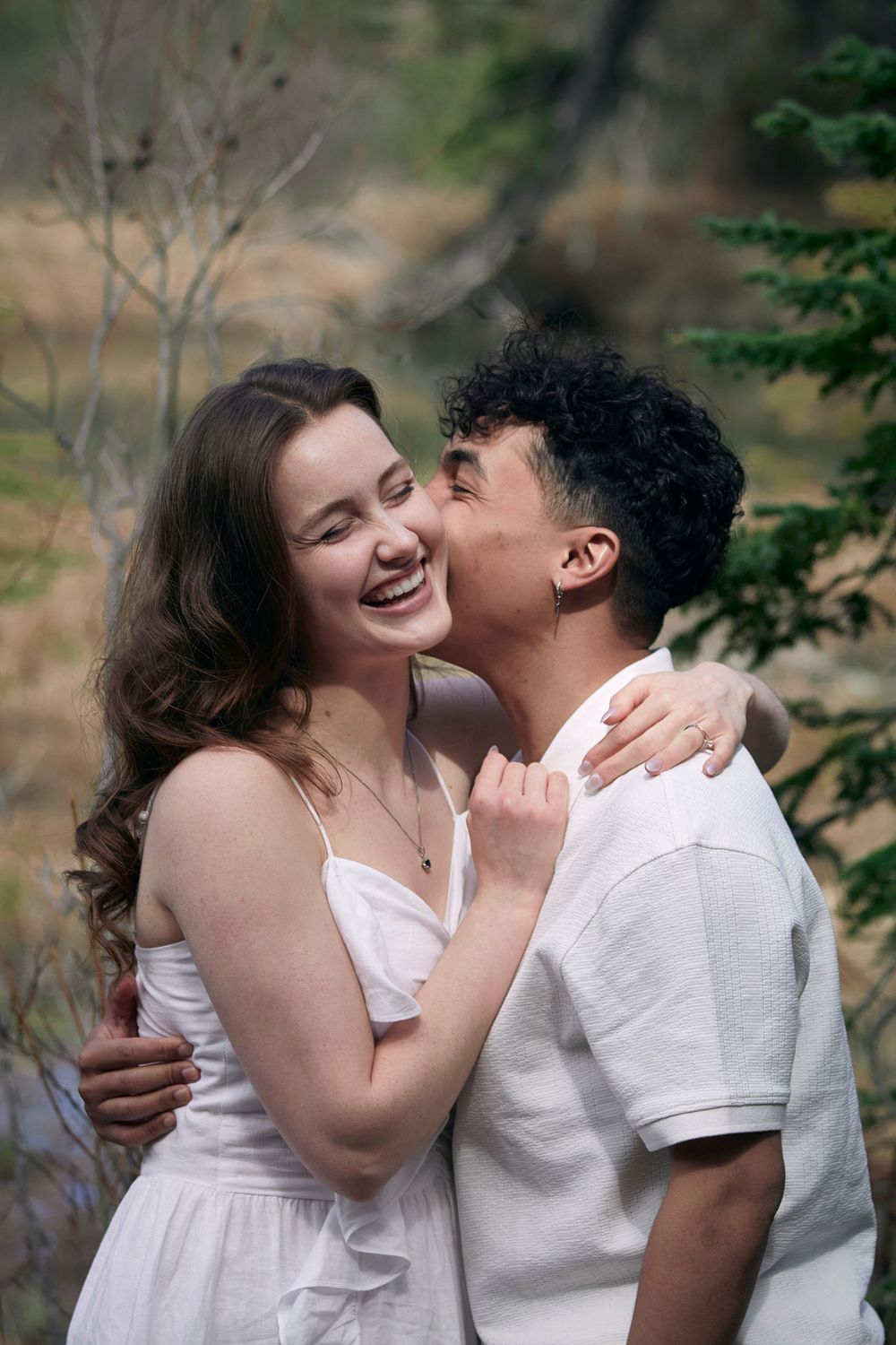 Engagement photoshoot. Young couple hugging in all white outfits. Man is kissing the woman's cheek.