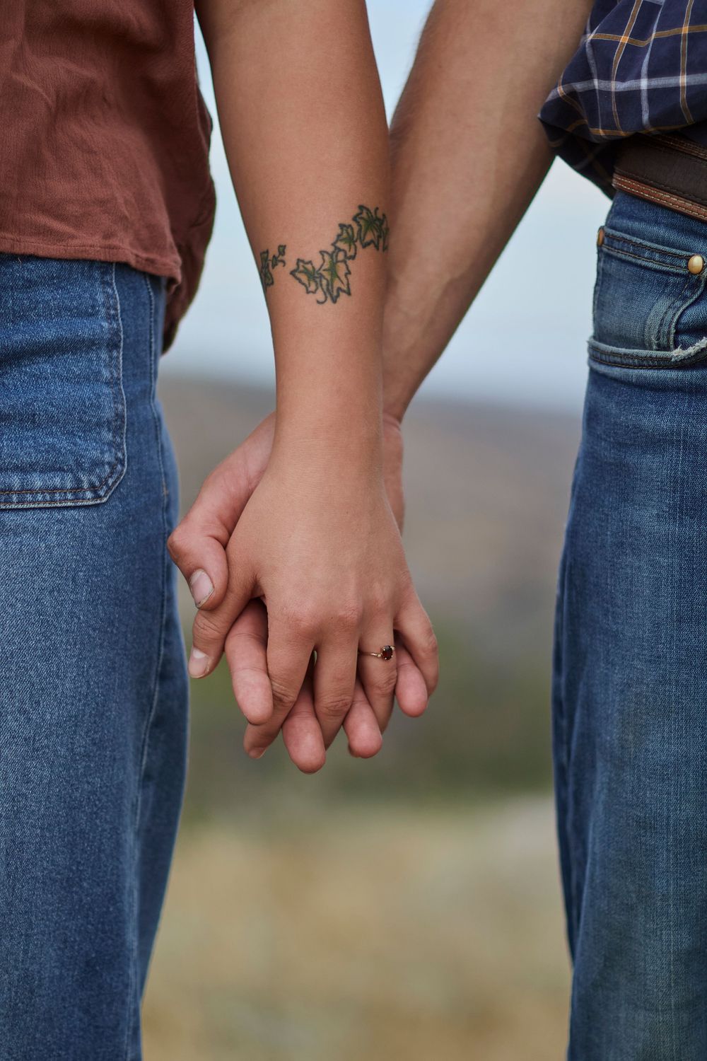 Couple holding hands outside by mountains. Girl with a tattoo