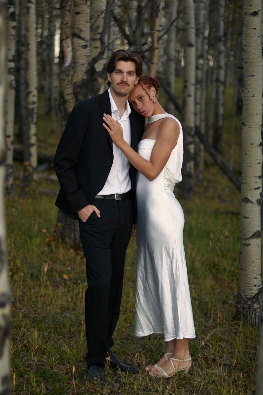 Wedding couple photography outdoor with soft light. Bride resting softly on grooms shoulder with her hand on his chest.