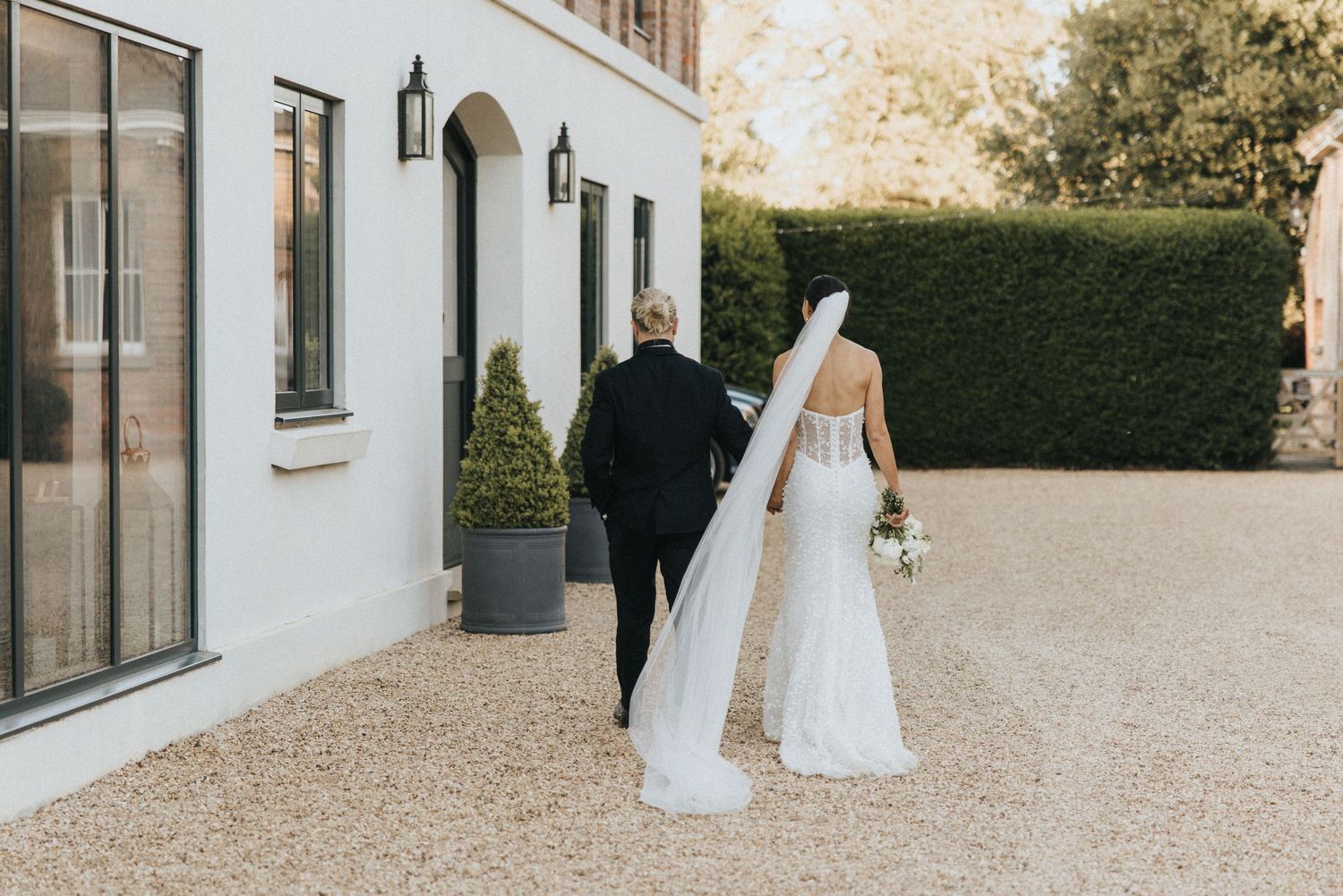 A bride and groom walk in wedding attire towards The Grange Leverton on a warm sunny day.