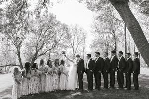 Black and white wedding party photo showing bridesmaids in floral dresses and groomsmen in dark suits lined up outdoors.