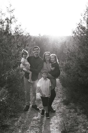 Black and white photograph of a family walking together through an orchard on a sunny day.