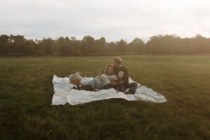 Group enjoying a sunset picnic on a blanket in a grassy field during golden hour.