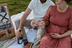 People enjoy drinks and appetizers at an outdoor picnic gathering with wicker baskets and casual attire.