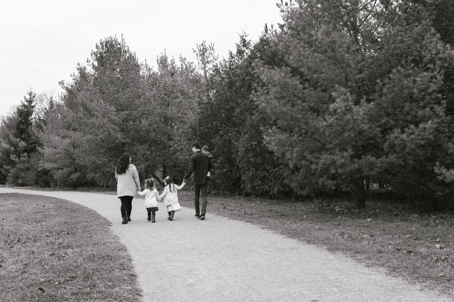 Black and white photo of a family walking together on a tree-lined path.