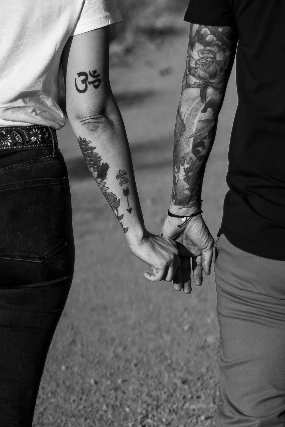 Close up of tattooed couple holding hands showing Om symbol and sleeve artwork.