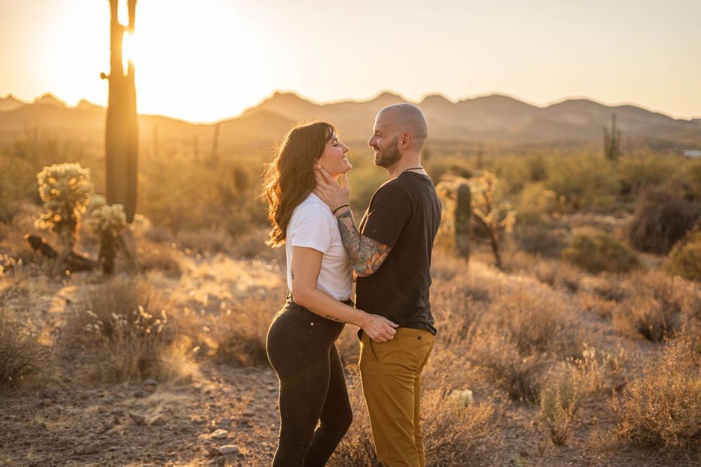 Couple laughing together in desert setting with mountains and saguaro cacti at sunset.