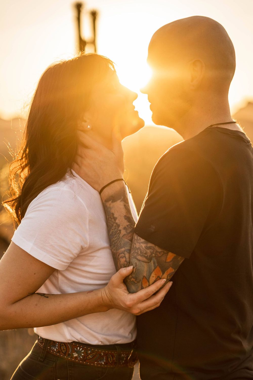 Couple sharing intimate moment at golden hour with visible tattoos.