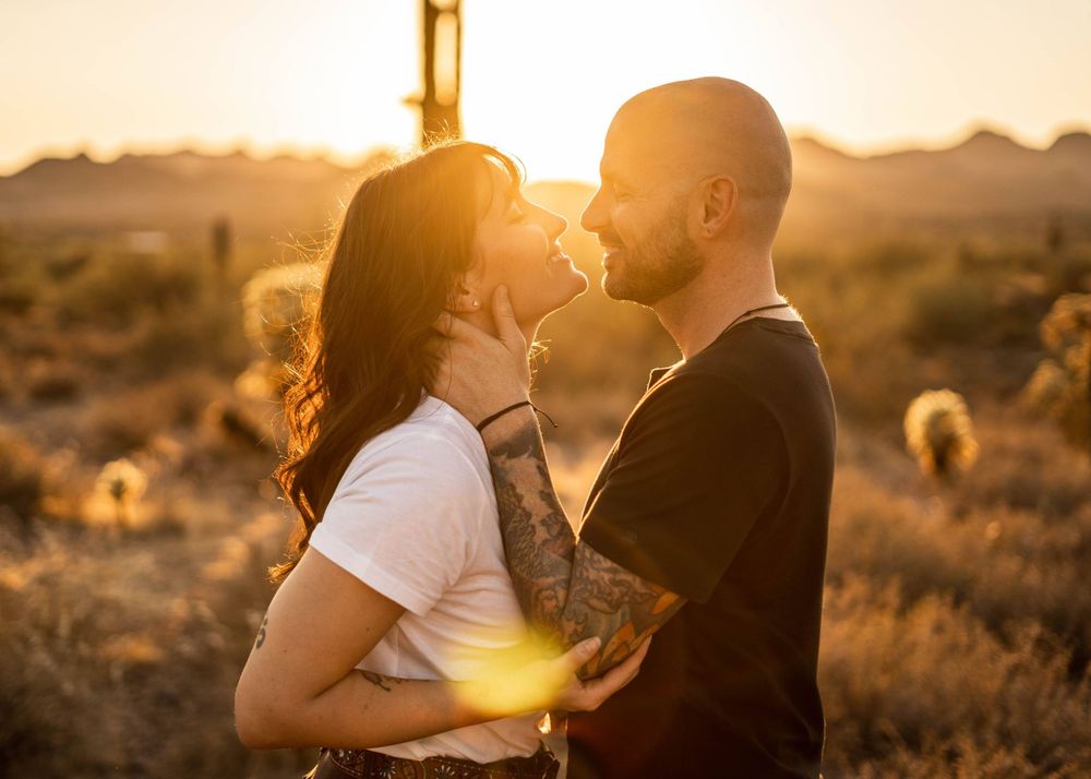 Couple embracing against desert landscape backdrop during golden hour with saguaro cactus.