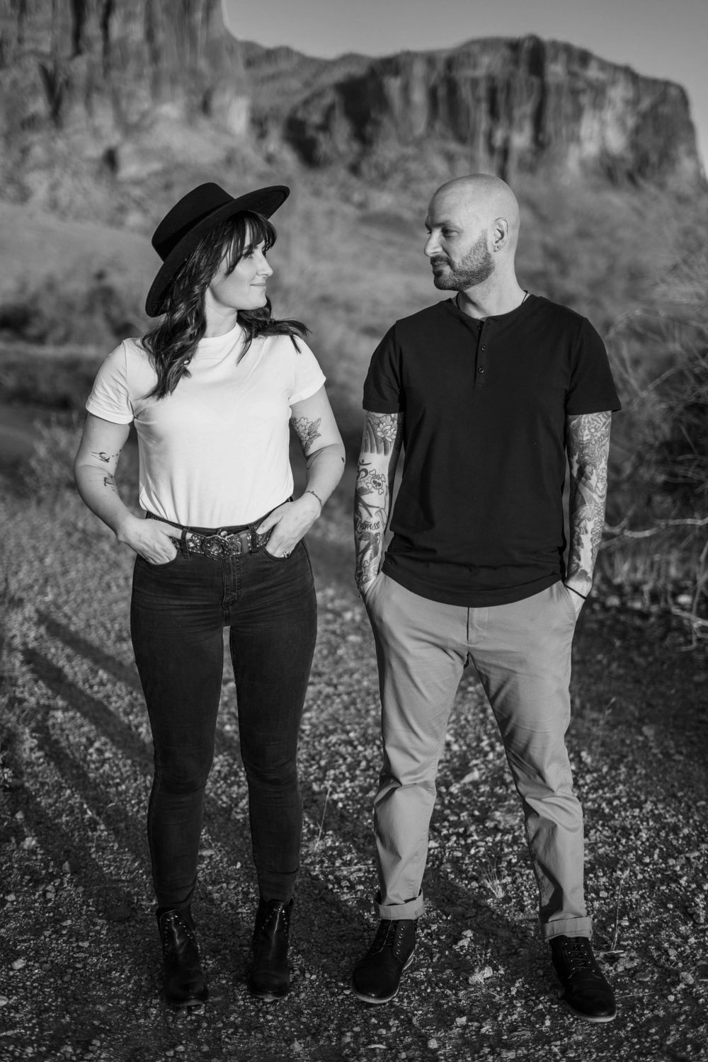Black and white portrait of couple standing in front of desert mountain landscape.