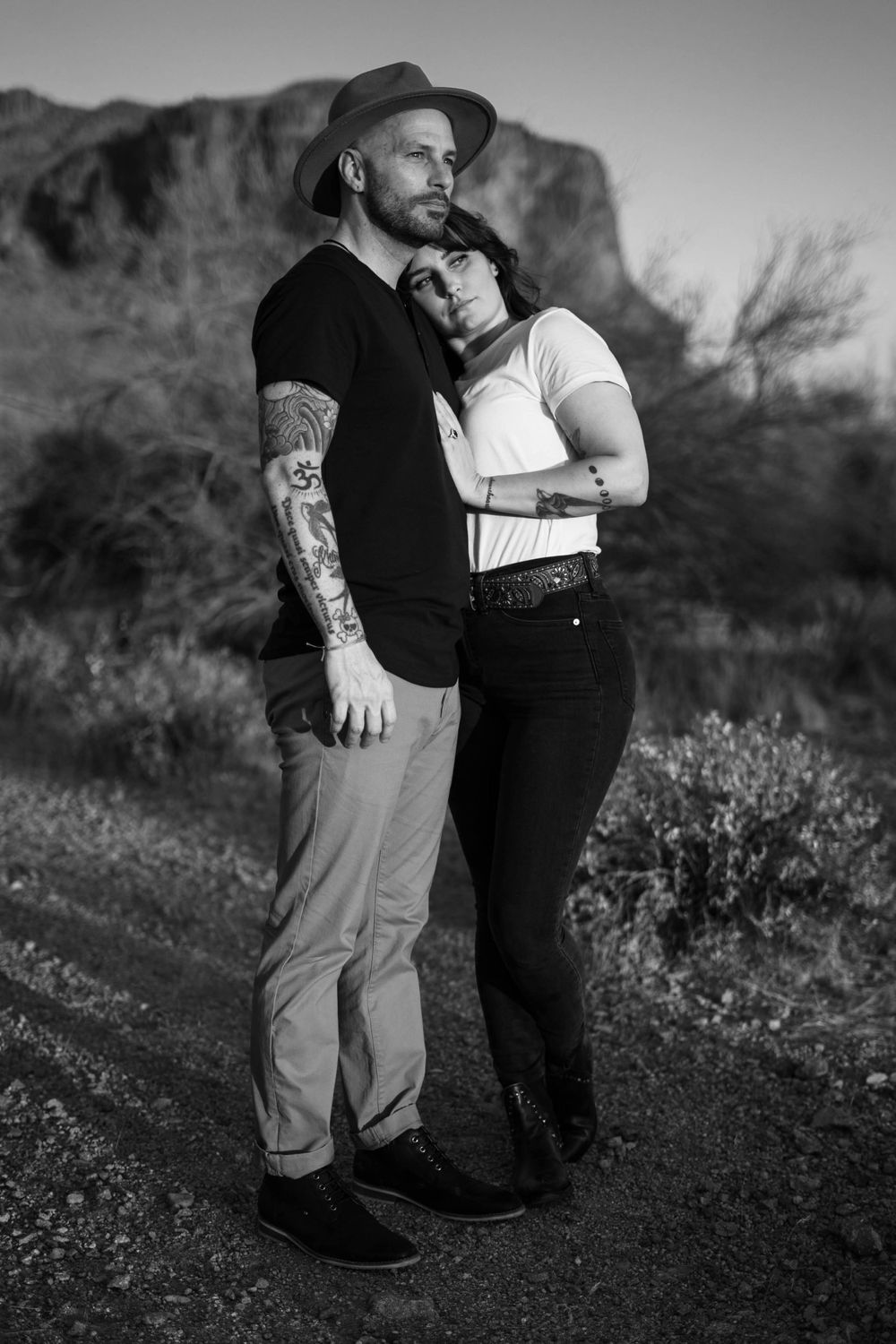 Black and white portrait of couple embracing outdoors with mountain backdrop.