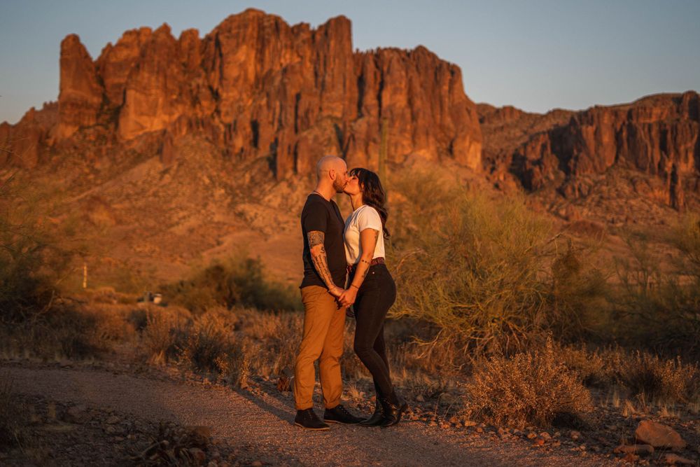 A couple shares an intimate moment at sunset with the dramatic Superstition Mountains in Arizona as their backdrop.