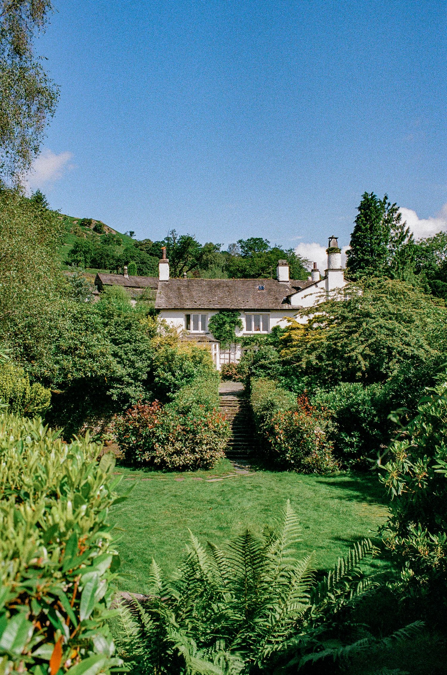 White cottage with beautiful manicured garden and flowering plants nestled in hillside setting.