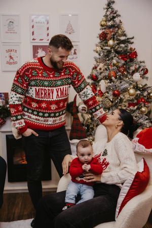 A family in festive sweaters share a holiday moment by the Christmas tree.