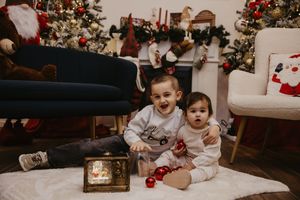 A festive Christmas scene with children sitting on the floor near decorated trees and holiday decorations.