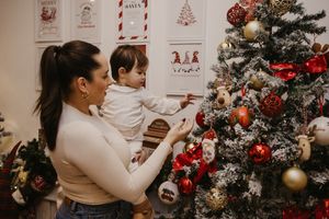 A decorated Christmas tree with red and gold ornaments stands next to a wall with festive holiday artwork.