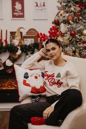 A festive holiday portrait with reindeer antlers and Santa pillow by a Christmas tree.